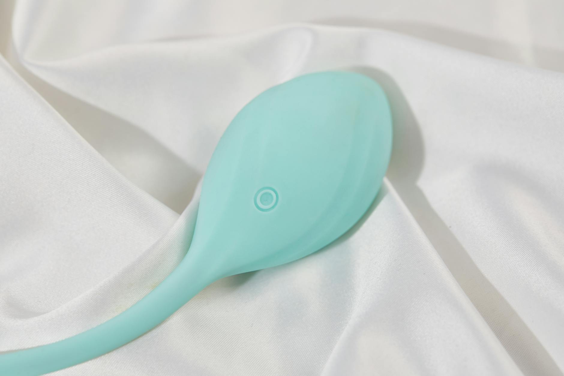 A stylish teal lemon vibrator on smooth white silk fabric, representing modern intimacy and self-care