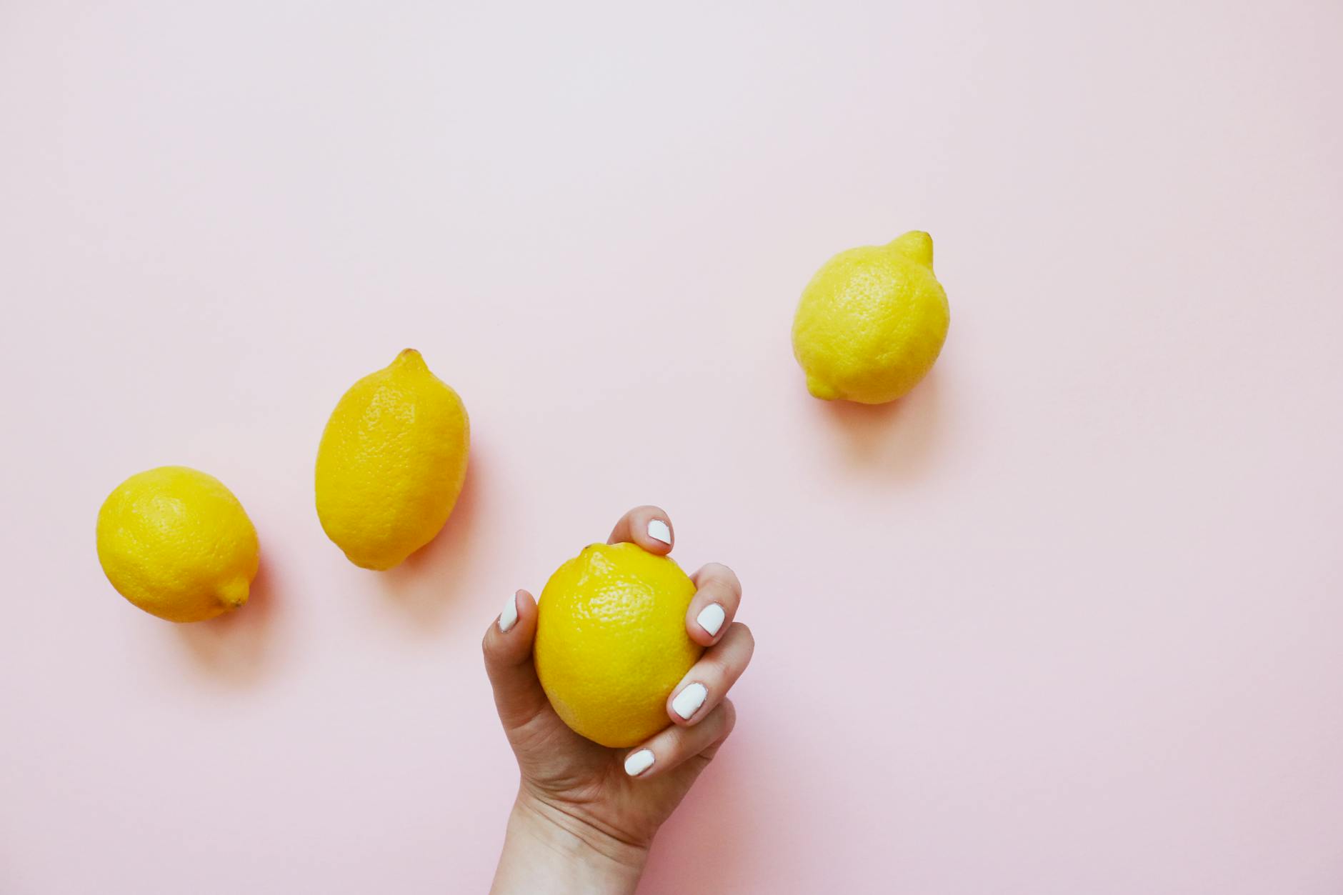 A hand holding a bright lemon on a soft pink background, symbolizing natural pleasure and wellness