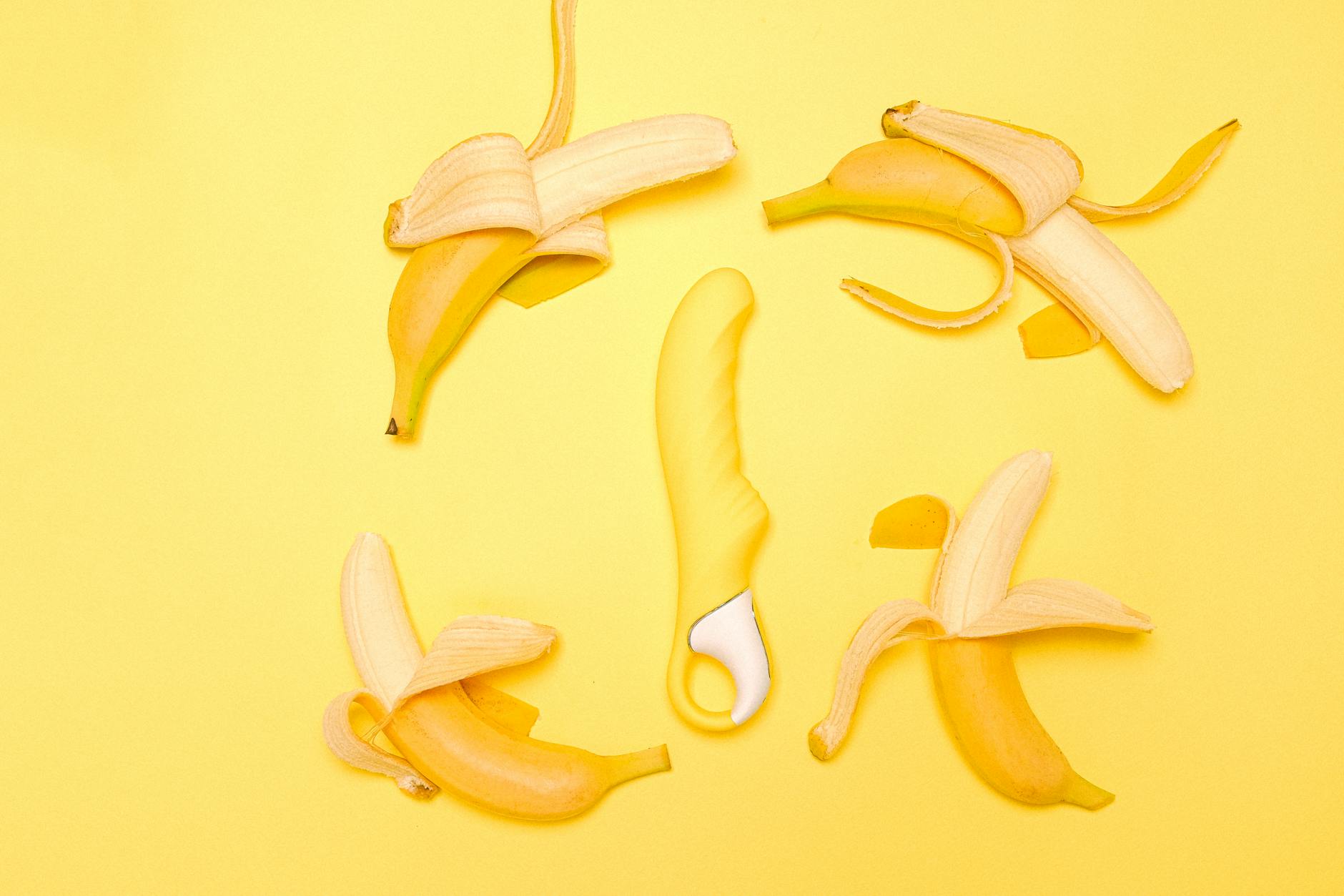 A yellow silicone lemon vibrator surrounded by fresh lemons on a bright yellow surface