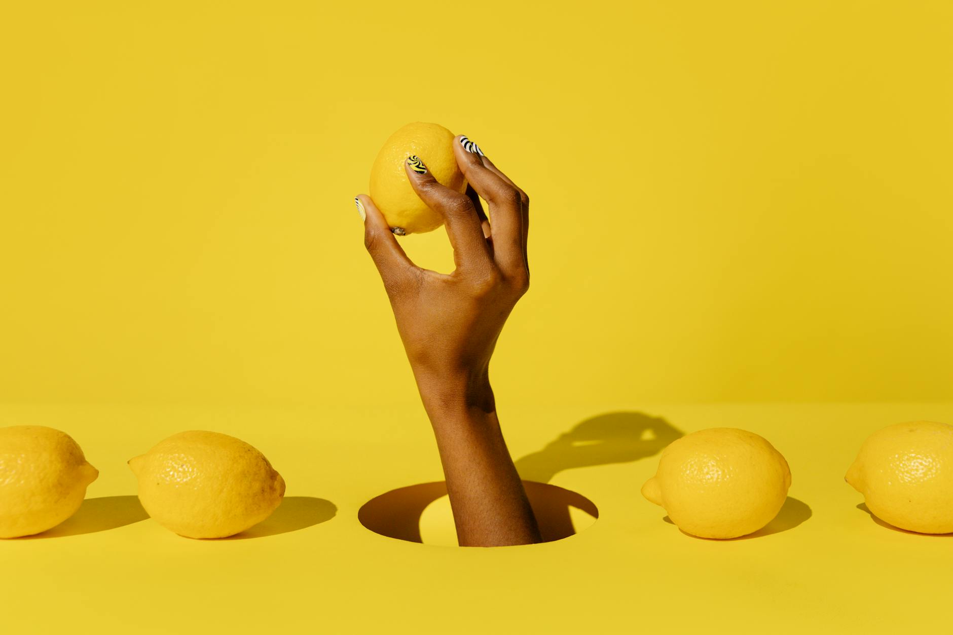 Hand holding a lemon against a vivid yellow background, symbolizing fresh sensation and citrus-inspired pleasure.