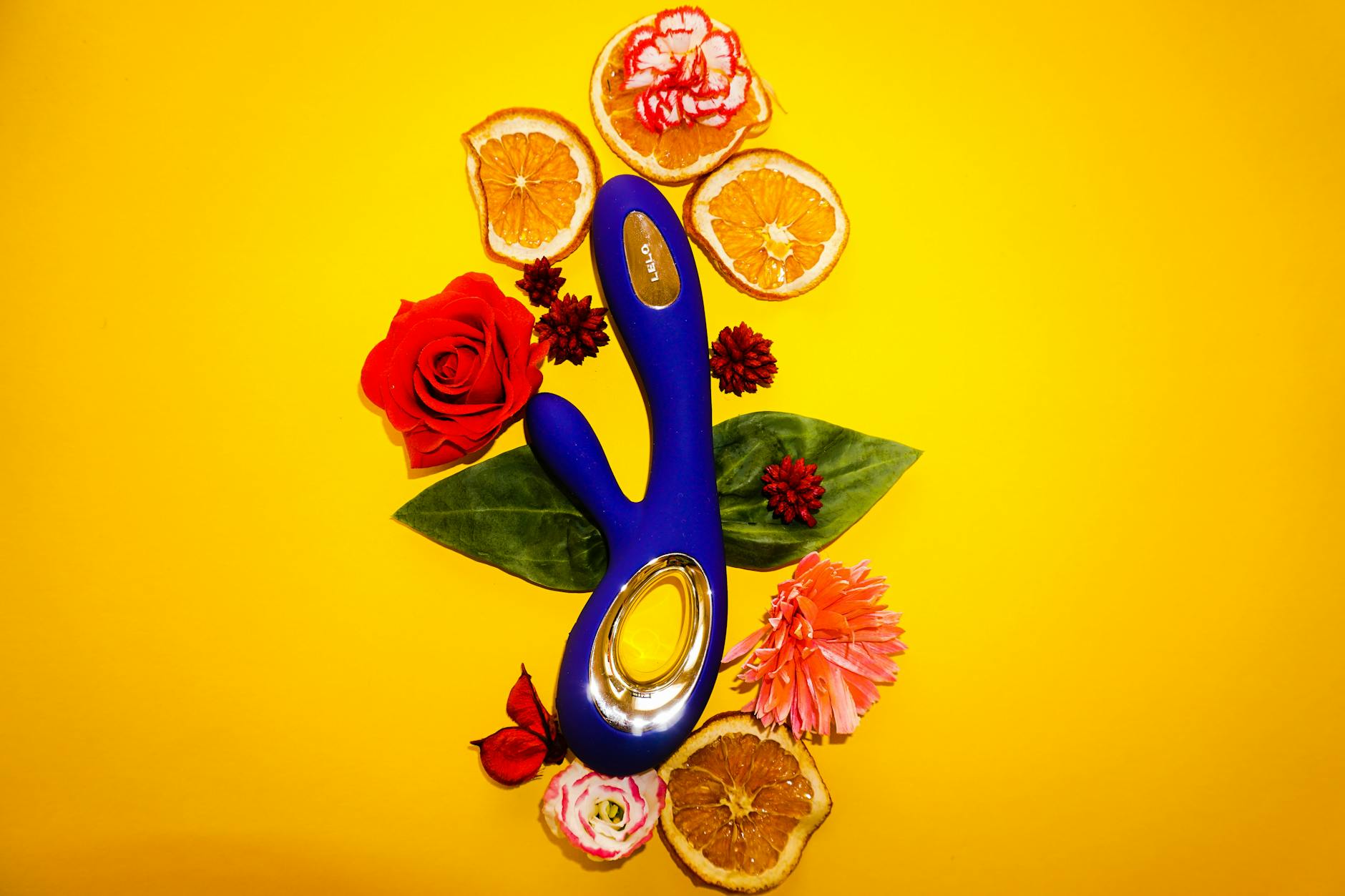 Bright lemon-colored vibrator surrounded by fresh citrus and flowers on a yellow background