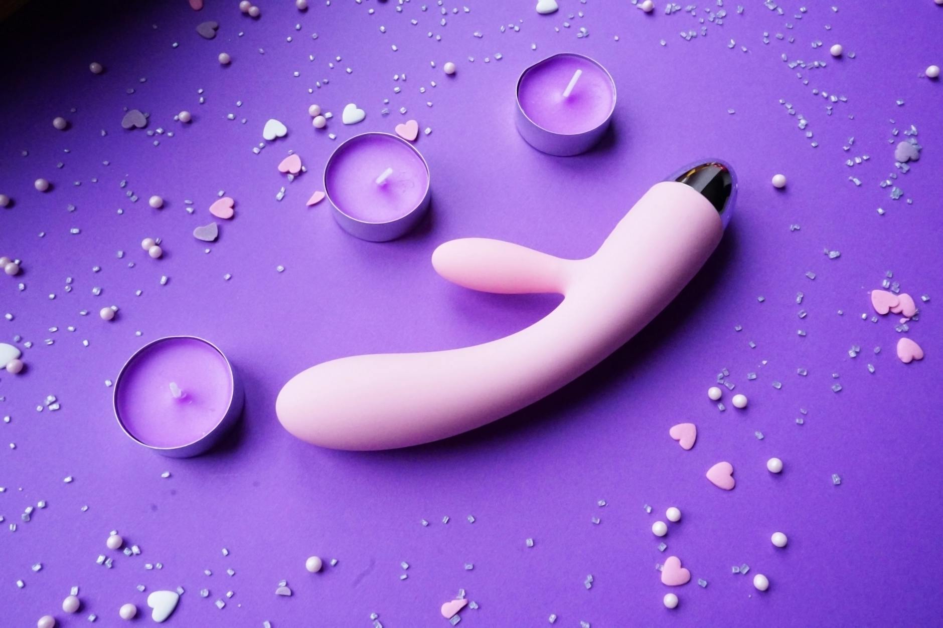 Pink vibrator on a purple background with heart confetti and candles, representing post-pleasure rest and recovery