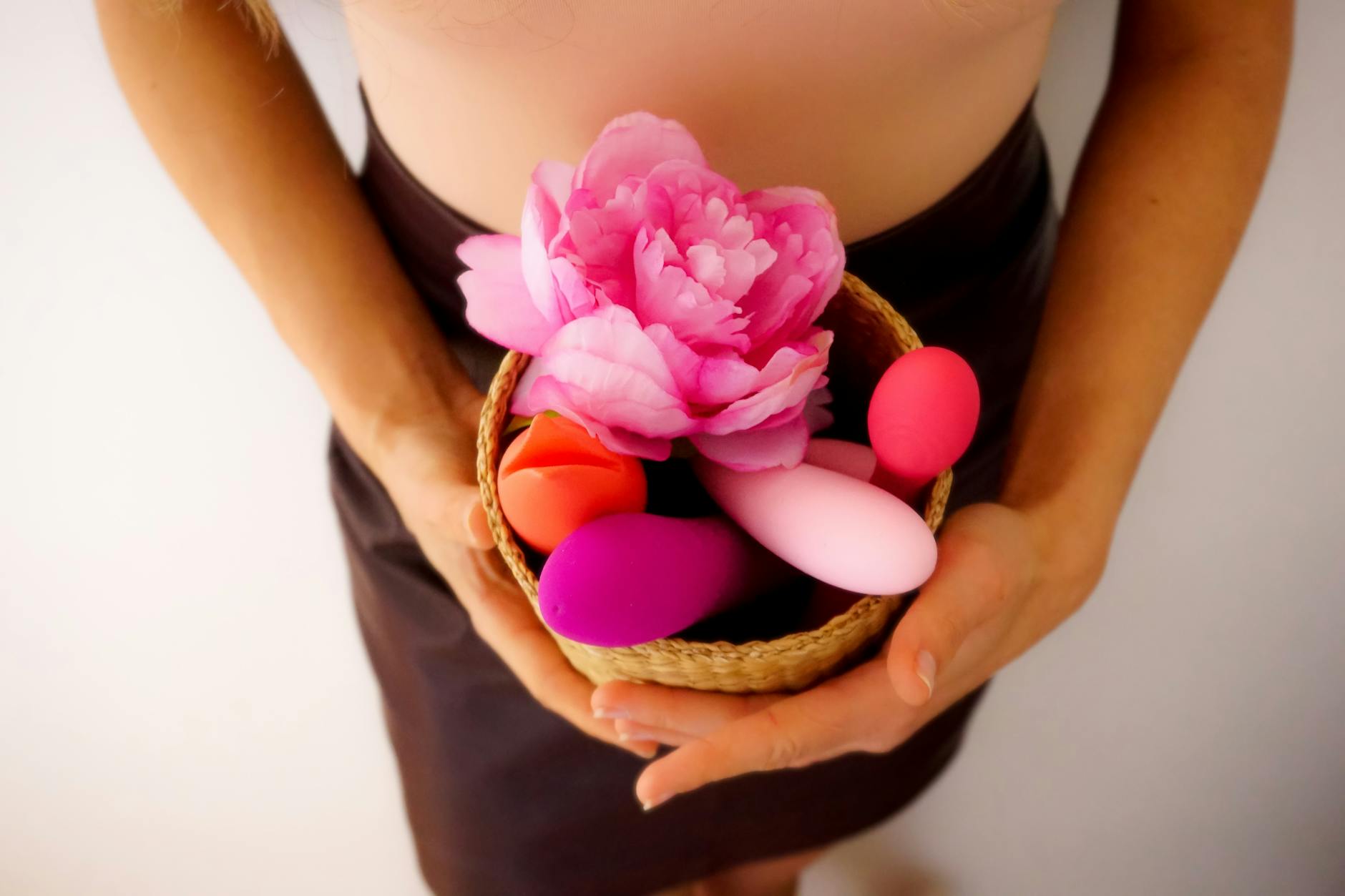 A close-up of a hand holding an orange vibrator against a minimalistic purple backdrop